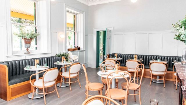 Interior modern de restaurant, cu pereți albi, mese și scaune din lemn, luminat natural