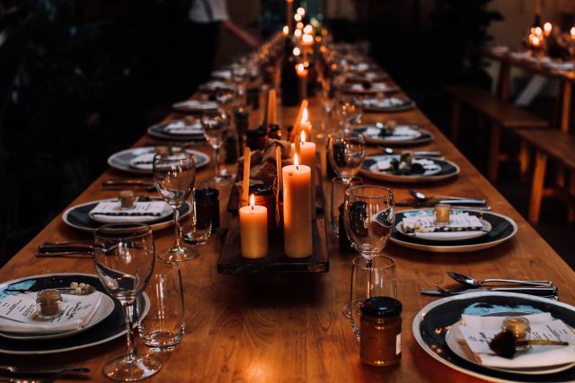 Masă lungă de restaurant pregătită pentru o cină aniversară, cu farfurii, pahare de vin și lumânări aprinse