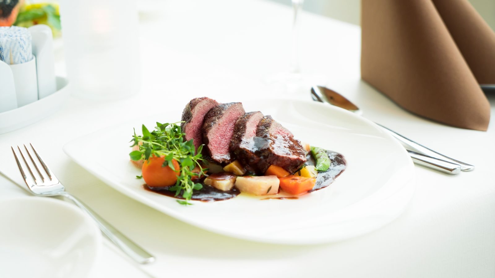 Felii de carne de vită rumenită, tăiate pe o farfurie, alături de garnitură de legume și sos