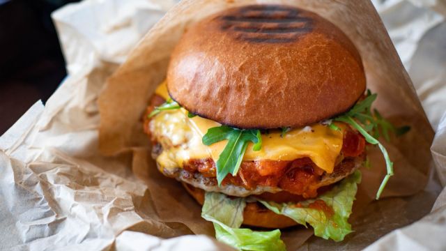 Burger gourmet cu brânză topită, salată verde și chiflă rumenită, fotografiat de aproape